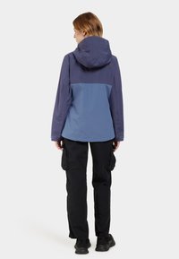 Lila und blaue wasserdichte Jacke mit Kapuze, elastischen Bündchen und lockerer Passform, kombiniert mit schwarzen Cargo-Hosen und Sneakers.