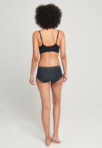 Svart bralette med justerbara band, tillsammans med mörkgrå boyshorts med spetsdekoration vid midjan och benöppningarna.