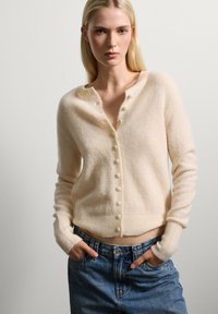 Cardigan beige chiaro realizzato in morbida lana, con scollatura rotonda, piccoli bottoni sul davanti e polsini e orlo a coste.