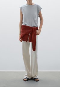 Harmaa lyhythihainen t-paita yhdistettynä kermaisiin leveälahkeisiin housuihin, jotka on kiedottu teksturoidulla punaisella neuleella, sekä mustiin liukusandaaleihin.