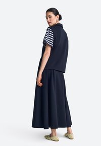 Tengerészkék ujjatlan felső csíkos rövid ujjakkal, hozzá illő, légies tengerészkék szoknya és világoszöld, díszes részlettel ellátott bebújós cipők.