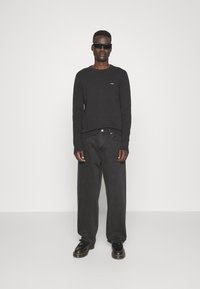 Maglione a coste nero con maniche lunghe, abbinato a jeans grigi scuri larghi e scarpe nere. Gli occhiali da sole completano l'outfit.