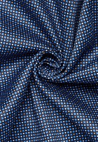 Tessuto blu navy con un motivo geometrico di quadrati azzurri e marroni. Texture liscia con una leggera lucentezza, disposta in una piega a spirale.