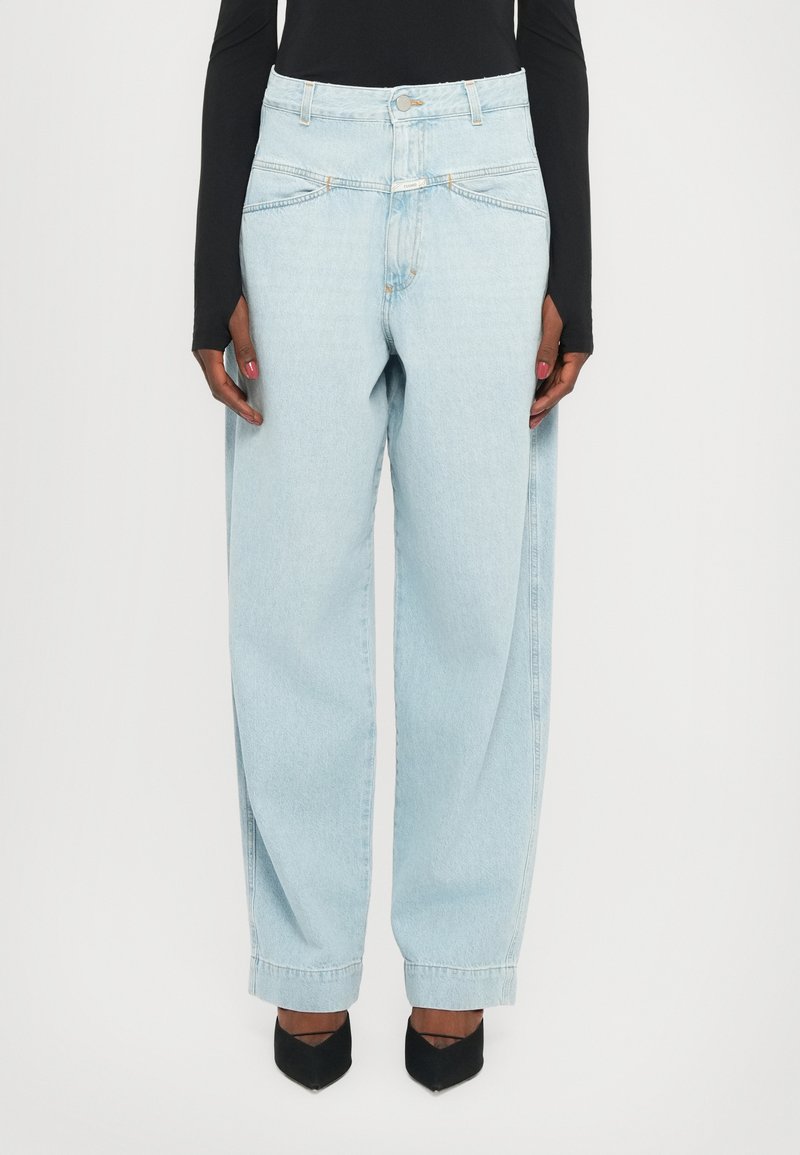 Jeans a vita alta di colore azzurro chiaro con vestibilità ampia, dotati di tasche frontali, cuciture chiare e chiusura con bottone. Indossati con tacchi neri.