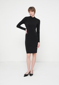 Vestido negro de manga larga con un diseño ajustado, con sutiles detalles de brillo en toda la prenda. Textura suave y largo hasta la rodilla.