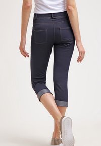 Mörkblå korta jeans med uppvikt fåll, som har två bakfickor och synliga sömnadsdetaljer. Materialet verkar elastiskt och glansigt.