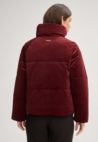 Giacca imbottita bordeaux con colletto alto, caratterizzata da una texture liscia e dal logo Joop! stampato sul retro. Realizzata in materiale morbido e vellutato.