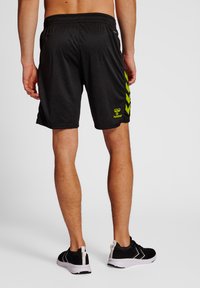 Zwarte sportshorts met groene chevronpatronen aan de zijkanten. Gemaakt van een lichtgewicht materiaal met een elastische tailleband.