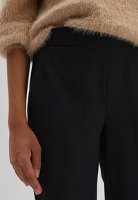 Pantalons noirs sur mesure avec une texture lisse, dotés de poches latérales et d'une coupe droite, associés à un pull beige moelleux.