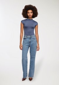 Granatowy bodysuit z krótkim rękawem w połączeniu z jasnoniebieskimi spodniami typu straight-leg oraz brązowymi szpilkami o spiczastym nosku, tworząc dopasowaną i luźną sylwetkę.