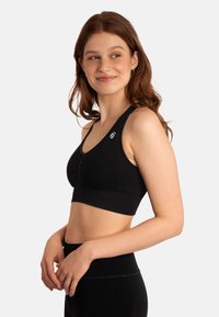 Zwarte geribde sportbeha met een V-hals ontwerp, voorzien van een plooidetail in het midden vooraan en een klein logo op de linkerschouderband.