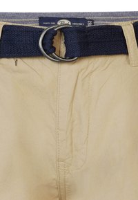 Pantalon khaki beige avec une ceinture tissée bleu marine. La ceinture est équipée d'une boucle circulaire en métal argenté, et le tissu a une texture lisse.
