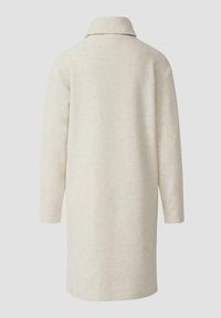 Długi, beżowy płaszcz z miękkiego materiału o minimalistycznym designie. Posiada kołnierz z zakładką i opuszczone ramiona. Brak widocznych zapięć.