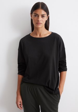 Zwarte lange mouw top, losse pasvorm met een ronde hals. Gemaakt van zachte stof, heeft iets drop shoulders, gecombineerd met donkergroene broek.