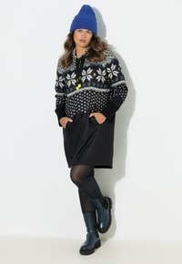 Sort hættetrøjekjole med snefnugmønster og lommer. Fremhævet med blå hue og sorte leggings, kombineret med blå ankelstøvler.