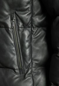 Zwart leren jack met een opvallende ritszak, gewatteerde textuur en gequilt ontwerp. Gladde afwerking met zichtbare stiksels.