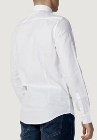 Camicia bianca a maniche lunghe con colletto classico, caratterizzata da una texture liscia e orlo dritto, abbinata a jeans in denim blu.