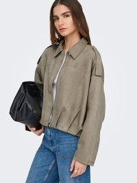 Khaki semsket jakke med glidelås foran, stor krage og senkede skuldre, kombinert med høyhøyde denim og en svart håndveske.