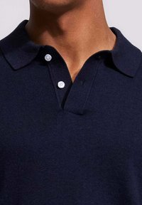Marineblauwe poloshirt van gebreide stof met een zachte textuur, voorzien van een klassieke kraag en twee witte knopen bij de halsopening.