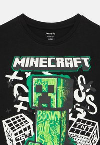 Czarny bawełniany t-shirt z zielono-białą grafiką inspirowaną Minecraftem, przedstawiającą Creepera, bloki oraz elementy tekstowe w różnych stylach.