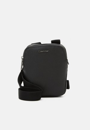 Borsa a tracolla nera in pelle con superficie testurizzata, chiusura con zip e tracolla regolabile. Presenta un logo Calvin Klein sul davanti.