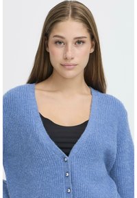 Cardigan lavorato a maglia di colore azzurro chiaro con scollo a V, maniche lunghe e bottoni argentati frontali. Texture morbida e motivo a costine.