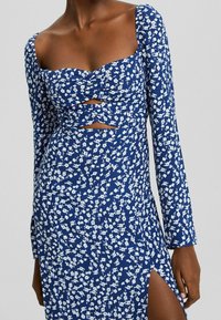 Blue floral dress with long sleeves, cut-out design at the waist, and side slit. Made of lightweight fabric, features small white flowers.