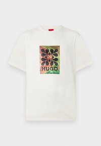 Λευκό κοντομάνικο Τ-shirt με πολύχρωμο αφηρημένο σχέδιο και μαύρα σχήματα πάνω από το κείμενο "HUGO" στο στήθος.