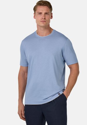 Light blue cotton t-shirt with short sleeves, round neckline, smooth texture, and subtle seam details. Paired with dark pants.