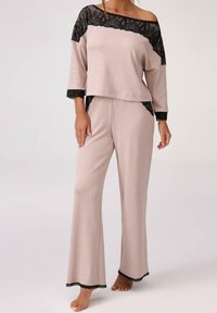 Jasnoróżowy zestaw odzieży do relaksu składający się z luźnej bluzki z czarnymi koronkowymi akcentami i dopasowanych szerokich spodni, o miękkiej fakturze i swobodnym fasonie.