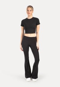 Sort cropped t-shirt og højtaljede, vidde leggings i stretchstof, bådet båret med hvide sneakers. Simpelt design, glat tekstur.