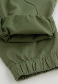 Zielone spodnie sportowe z gumkami na mankietach, wykonane z gładkiego, elastycznego materiału. Posiadają marszczoną talię oraz subtelne detale przeszycia.