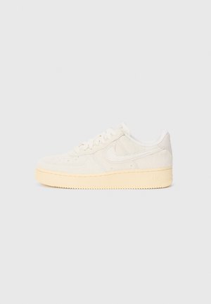 Baskets basses blanches avec semelle crème, fermeture à lacets, panneaux cousus et logo Nike swoosh sur le côté, présentées en profil droit sur fond gris.