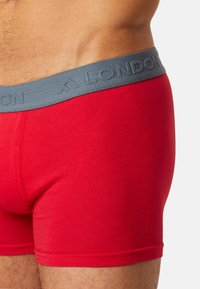 Red cotton boxer briefs with a grey elastic waistband featuring embossed letters "LONDON." Close-up view highlights fabric texture and fit.