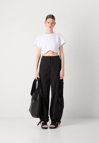 Κοντομάνικη λευκή μπλούζα, μαύροι παντελόνες cargo με φαρδιά γραμμή και τσέπες, μαύρες επίπεδες σαγιονάρες και μια μεγάλη μαύρη τσάντα ώμου.