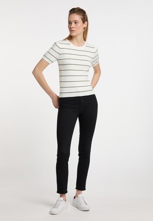 Weißes Kurzarmhemd mit grünen horizontalen Streifen, kombiniert mit schwarzen, eng anliegenden Jeans und weißen Sneakers. Einfache Stricktextur, Rundhalsausschnitt.