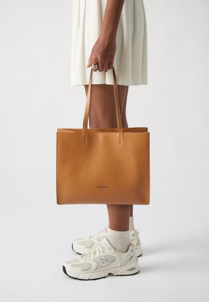 Borsa a spalla in pelle marrone chiaro con design minimalista, struttura piatta e due manici. Presenta un piccolo logo impresso sul davanti.