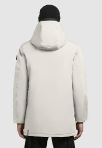 Hvid isoleret parka med hætte, der har en glat tekstur og en let glans. Sort beanie bæres, med et logo på bagsiden.