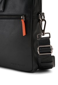 Black leather bag with a zippered compartment, featuring an orange zipper pull, silver hardware, and a textured strap with a logo.