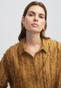 Tan, sheer shirt with textured vertical stripes and frayed edges. It features a collar and button-up closure.
