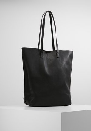 Bolsa de mano de cuero negro texturizado con dos asas largas, de pie sobre una superficie blanca contra un fondo gris claro.