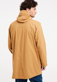 Chaqueta impermeable marrón con capucha, que presenta un corte relajado, una textura suave y un logotipo sutil en la parte superior de la espalda.