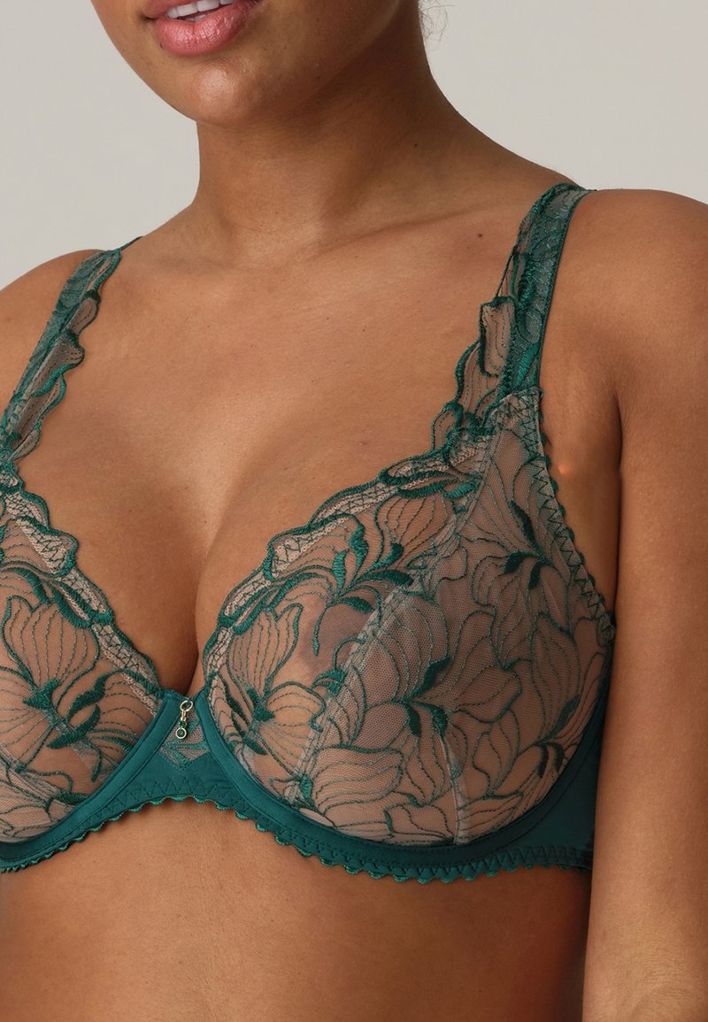 Soutien-gorge en dentelle teal avec broderie florale, bonnets transparents, bords festonnés, bretelles ajustables et une fermeture à crochets avec un petit charme décoratif.