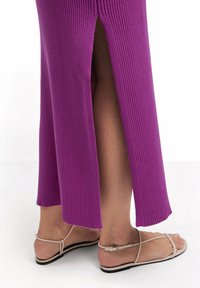 Lila geripptes Strickkleid mit seitlichen Schlitzen, kombiniert mit beigen Sandalen mit Riemchen. Das Kleid hat eine eng anliegende Silhouette und Texturdetails.