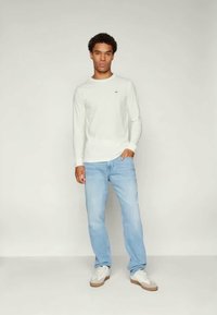 Λευκό μακρυμάνικο μπλουζάκι συνδυασμένο με ανοιχτό μπλε τζιν. Το σύνολο συμπληρώνεται από λευκά αθλητικά παπούτσια με ανοιχτό καφέ σόλες.