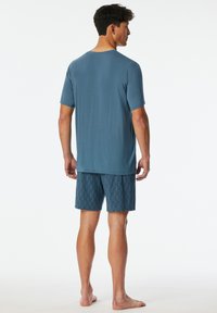 Das Schlafanzugset für Herren besteht aus einem hellblauen Kurzarmhemd und gemusterten Shorts mit einem geometrischen Design, gefertigt aus weichem Stoff.