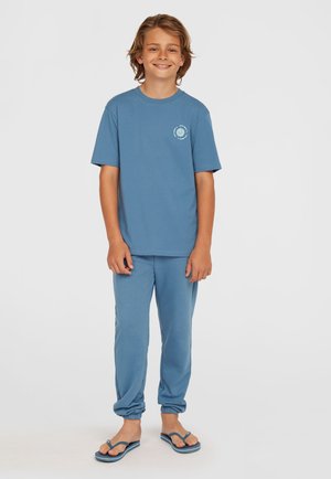 Blauwe katoenen t-shirt en bijpassende joggers, met een kleine graphic op de borst, gecombineerd met blauwe flip-flops. Zachte textuur, ontspannen pasvorm.