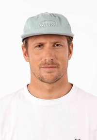 Casquette en velours côtelé bleu clair avec le logo brodé "OXBOW" à l'avant. Texture douce, forme arrondie et visière plate. Portée avec un t-shirt blanc.