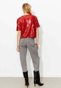 Haut en sequins rouges à manches courtes associé à un pantalon gris taille haute et des bottines à talons noires. Texture lisse et contraste de couleurs vives.