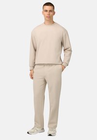 Béžová, ľahká mikina a zodpovedajúce nohavice vyrobené z jemného materiálu. Dizajn sa vyznačuje jednoduchým, voľným strihom a rebrovanými manžetami.